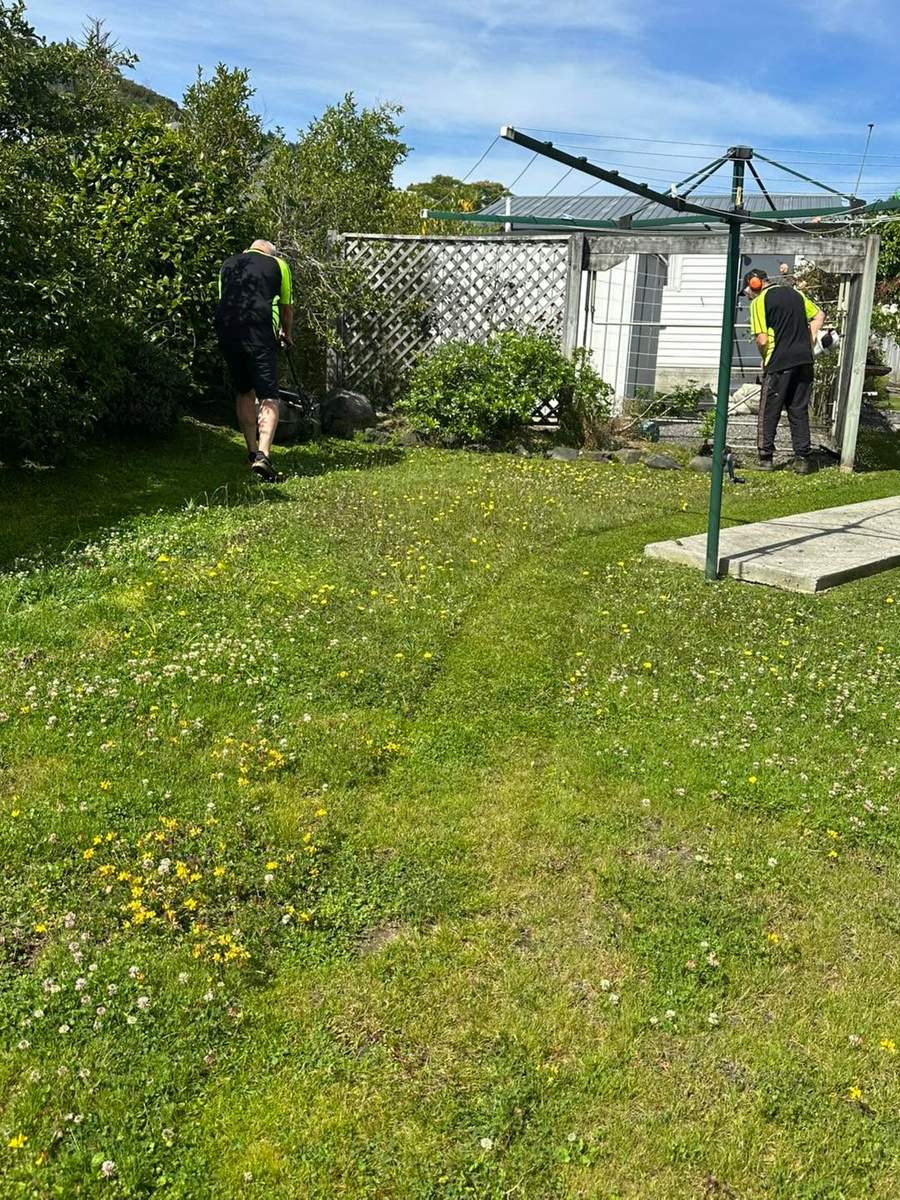 Two team members mowing and trimming a flowery lawn